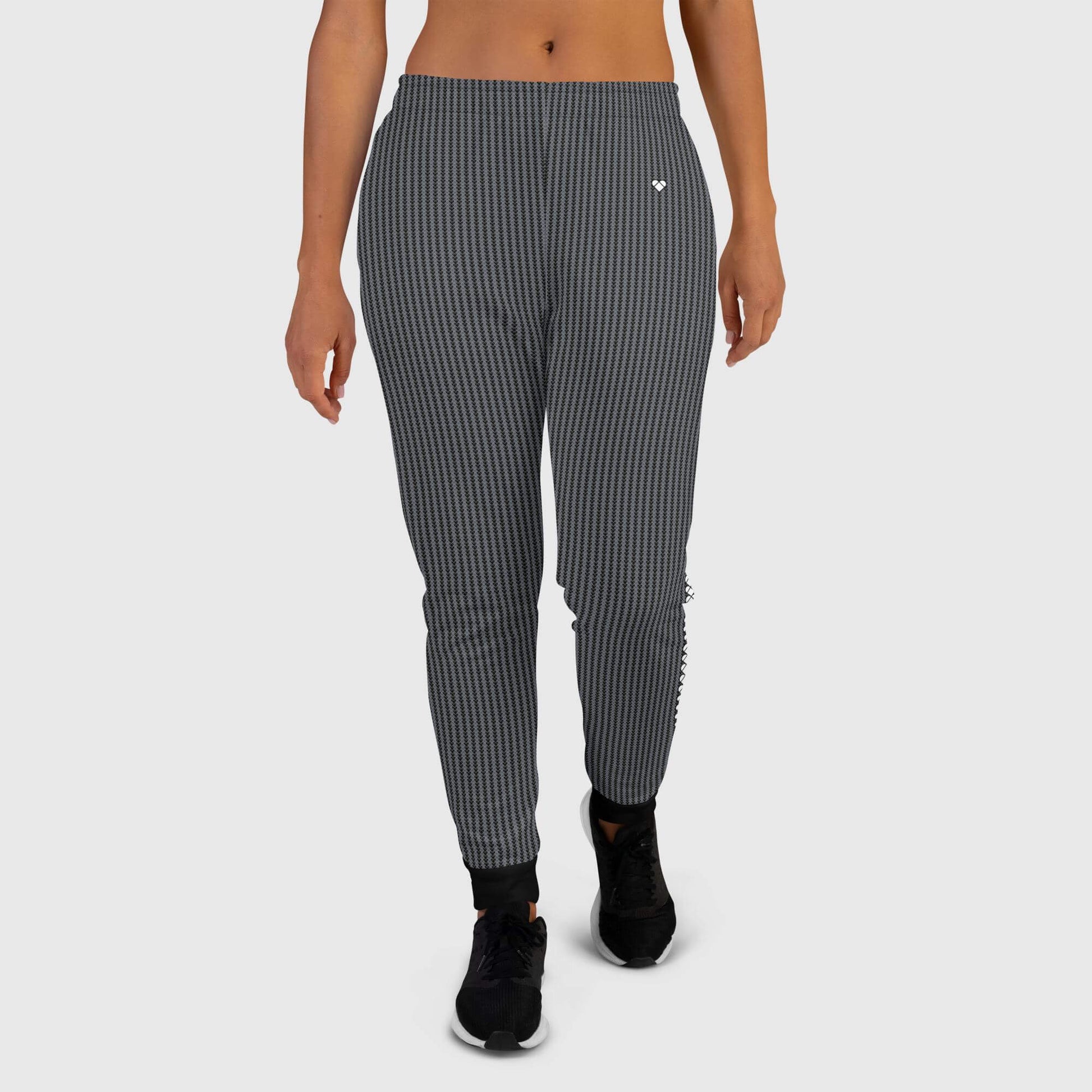 A pair of black joggers for women, with a heart-shaped pattern in shades of grey and a black stripe with brand hearts along the legs, practical pockets, and a brushed fleece inside, front view